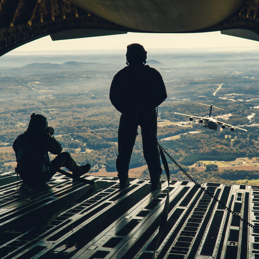 Voice for Valor host Michael Komorous photographing from the open ramp of a C-17 Globemaster III with another aircraft in formation — veteran interview podcast