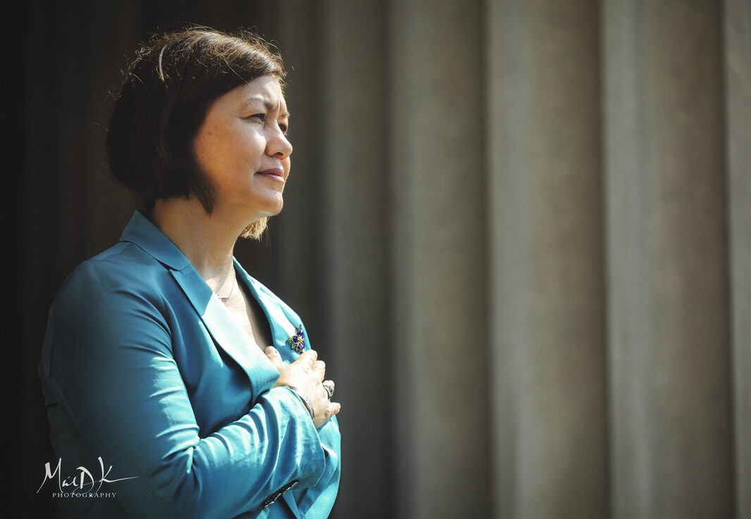 A guest stands with her hand over her heart against the columns of the National Archives Building during the Fourth of July ceremony.